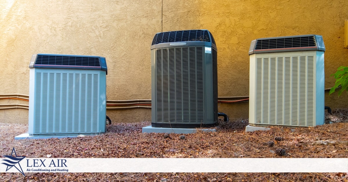 Three air conditioners next to one another on the ground outside of a yellow wall