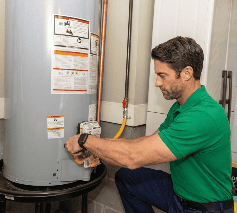 A man in a green shirt adjusts the valve on a water heater in a utility room.